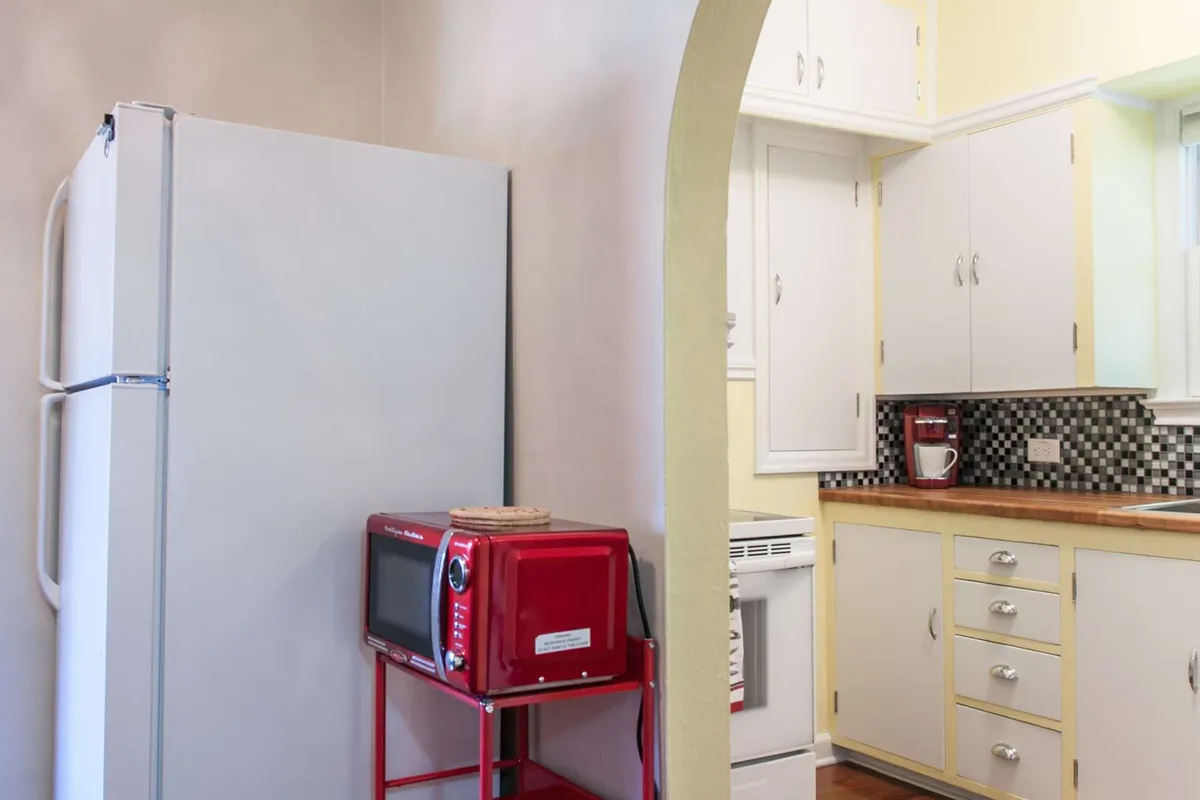 This image captures the heart of the kitchen, featuring a prominent refrigerator, a distinctive red microwave, and a countertop with a sink. The scene conveys a welcoming, functional space suitable for preparing meals, baking, and family gatherings. The setup highlights modern appliances integrated into a warm, vintage-inspired design.