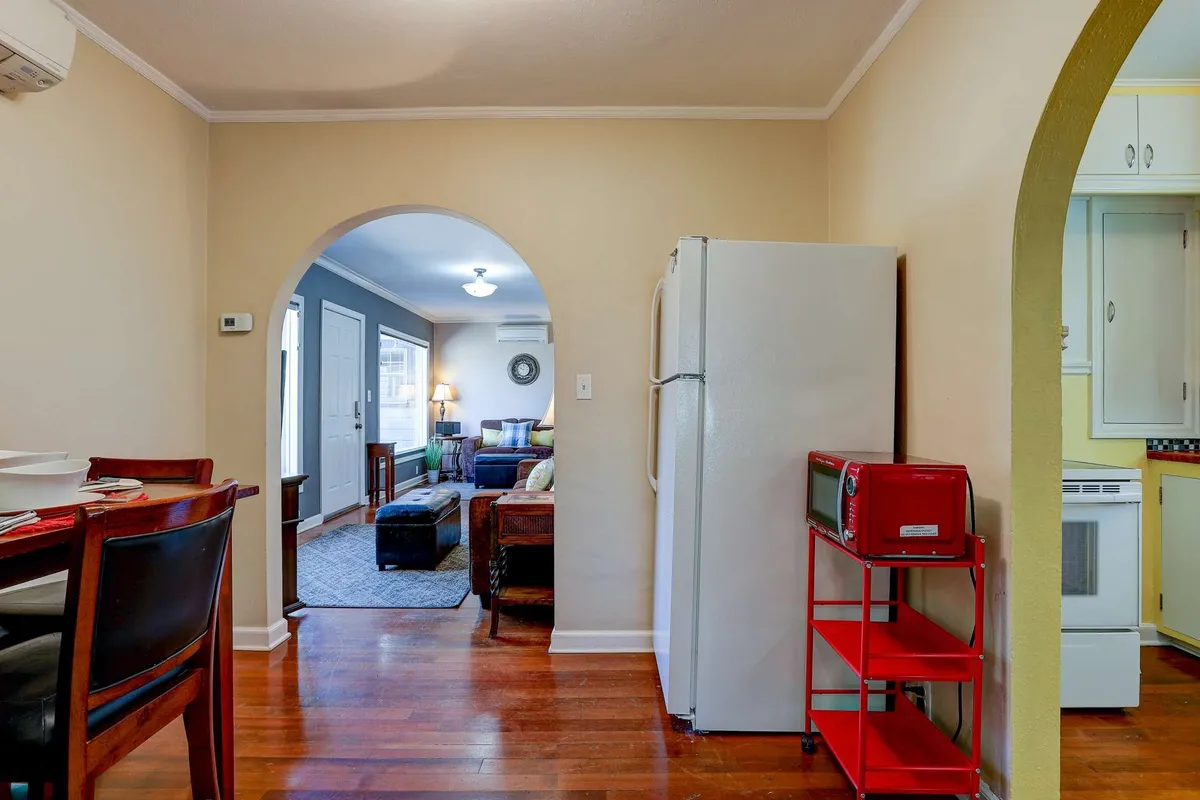 A cozy dining table with chairs set under an arched doorway, adjacent to the kitchen with a refrigerator and a red microwave. The scene is ready for family meals or entertaining guests, exuding warmth and hospitality.