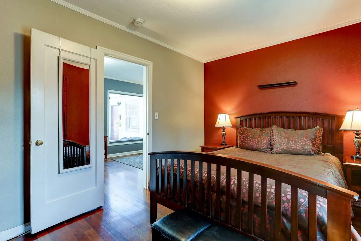 A bright bedroom with patterned bedding, bedside tables with matching lamps, and a mirror on the door. Sunlight streams into the room, enhancing the comfortable and warm mood, perfect for relaxing or reading before bed.