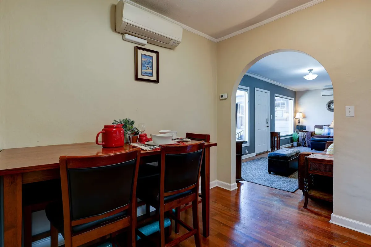 A warm dining area with a wooden table and chairs, viewed through an arched doorway that offers a glimpse of the adjoining living space. Natural light floods in, enhancing the inviting feel and sense of openness.