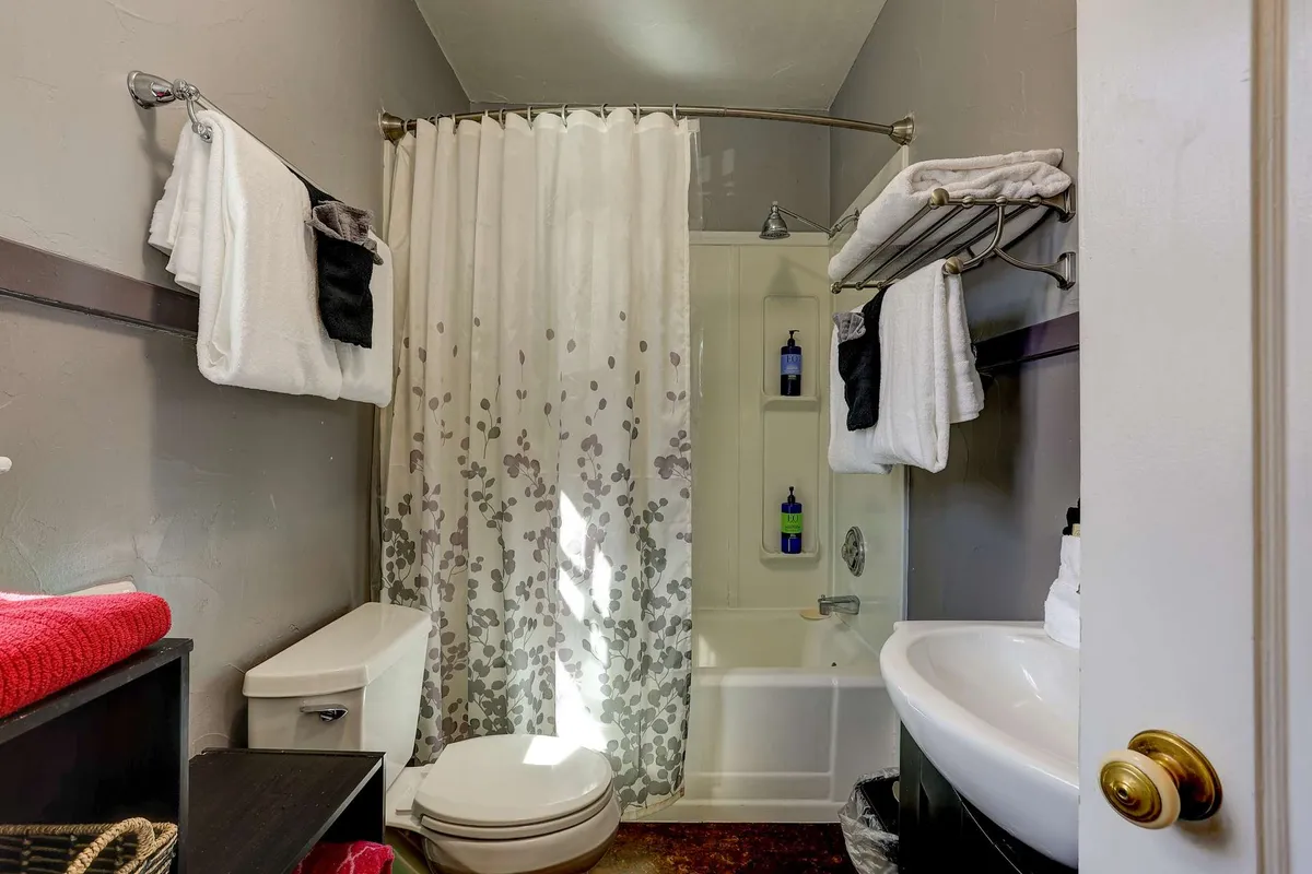 A bathroom with a clean bathtub, vanity, shower curtain, and fresh towels arranged neatly. The setting is calm and rejuvenating, conveying cleanliness and comfort—ideal for a refreshing shower or a relaxing bath after a day of adventure.