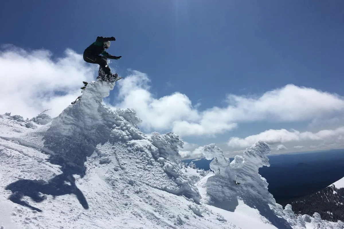 An exterior action shot captures a snowboarder mid-air against a snow-capped mountain and vibrant blue sky. The scene is lively and outdoorsy, evoking the spirit of exploration and adventure accessible near the cottage.