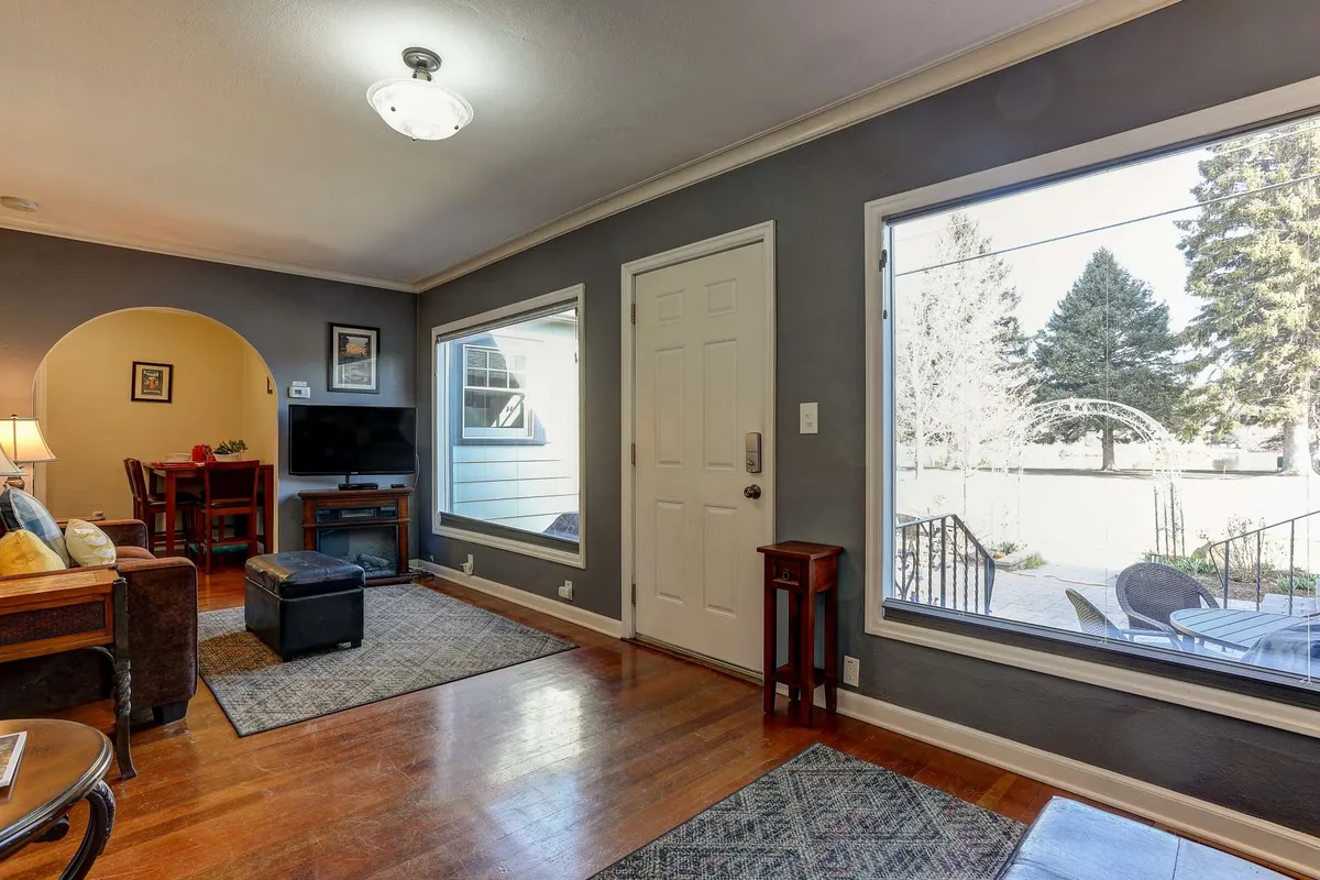 This image showcases the cottage’s entrance area with large windows, a door leading outside, wooden furniture, and soft natural lighting. The inviting setup connects the cozy retreat to the vibrant world just outside the door.