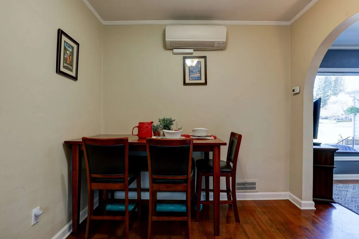 Pictured is a tidy dining area with a wooden table, several chairs, eye-catching wall art, and an air conditioning unit. The setup is ideal for meals, informal work sessions, or reading, fostering a versatile environment well-suited to remote work needs.