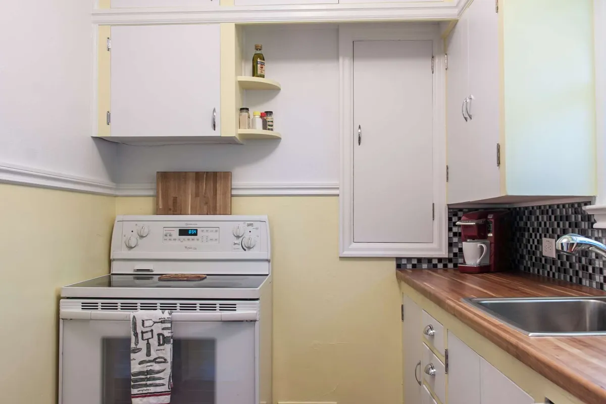 This image focuses on the stove and kitchen sink set against a wooden countertop. The mood is cozy and homely, with an emphasis on meal preparation and the warmth of sharing food with others. The vintage feel is enhanced by the classic design elements and muted tones.